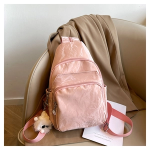 Detailed view of pink pleated chest bag with soft matte texture and white plush charm