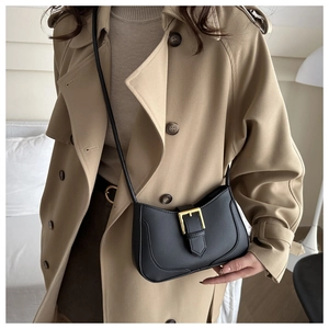 Détail d'un sac demi-lune noir sur un trench-coat avec boucle dorée et bandoulière