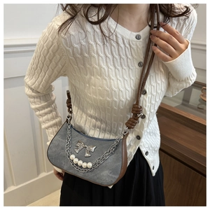 Close-up of blue denim shoulder bag with silver bow, pearls, and metal chain detail