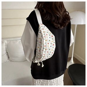 Close-up of white canvas chest bag featuring colorful polka dots and adjustable strap
