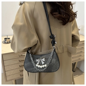 Close-up of crescent shoulder bag with metallic bow, pearls, and double silver chains