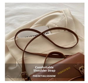 Détail de la bandoulière en cuir et des boucles dorées d'un sac besace marron