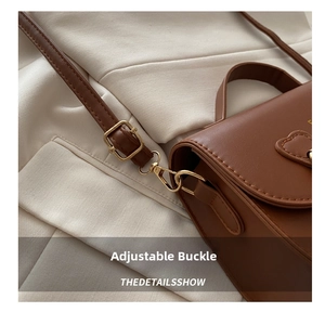 Détail de la bandoulière réglable avec boucle dorée et décor cœur sur le sac brun