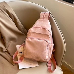 Pink waterproof nylon crossbody chest bag with plush bear charm on a beige seat