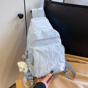Light blue pleated nylon chest bag with triple zipper pockets and plush ball charm