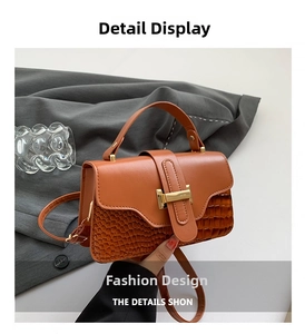 Detail of a brown two-tone crossbody bag with crocodile texture and gold hardware