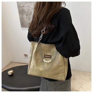 Detail of khaki tote bag featuring a silver chain, white pearls and a leather brand label