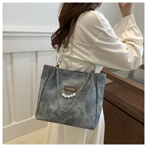 Detail of gray vintage washed canvas tote bag with chain strap and pearl accents on model