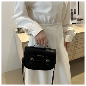 Détail du sac selle en cuir noir mat avec boucles dorées et lettrage de mode chic