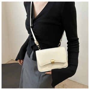 Detail view of a white leather crossbody bag featuring a golden buckle and adjustable strap