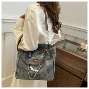 Detail of gray canvas tote bag with pearl chain accents and brown leather handles