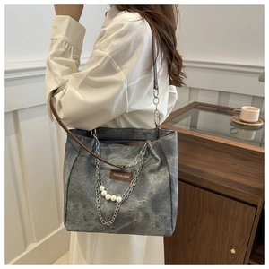 Detail of grey vintage tote bag with metal chains, white pearls and brown leather strap