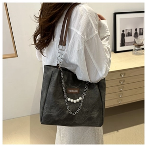 Detail of grey tote bag with elegant large pearl chain and brown leather logo patch