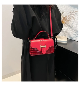 Detail of red crossbody bag with crocodile pattern and golden metal buckle on black coat