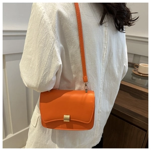 Detail of minimalist orange leather flap bag with gold clasp worn over a white coat
