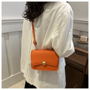 Side view of a bright orange leather crossbody bag worn with a white shirt and metal clasp