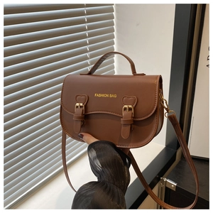 Détail du sac selle marron café avec rabat ondulé et boucles dorées en forme de cœur