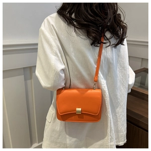 Detail shot of bright orange leather crossbody bag with a gold rectangular metal buckle