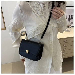 Detail of elegant black crossbody bag featuring a classic gold square metal buckle closure
