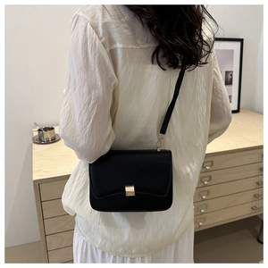 Minimalist black rectangle flap bag with gold clasp shown worn as a crossbody shoulder bag