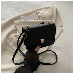 Detail of black leather crossbody bag with gold hardware on beige suit jacket