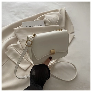 Detail of white leather shoulder bag with a gold metal clasp on a beige blazer background