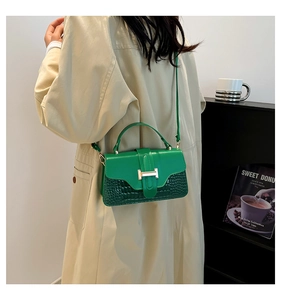 Detail of green leather handbag with gold H buckle worn over a beige trench coat