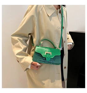 Detail of green crocodile texture leather handbag with gold H-clasp on beige coat