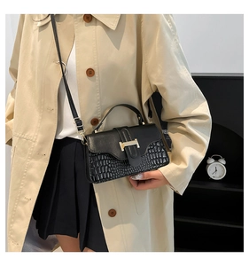 Detail of black crocodile texture handbag with gold buckle on a beige trench coat
