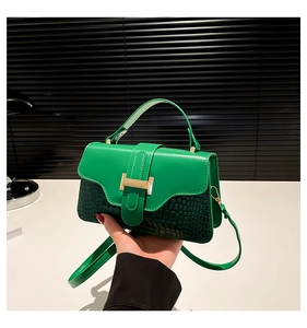 Detail of green leather handbag featuring mock croc texture and gold H-shaped clasp