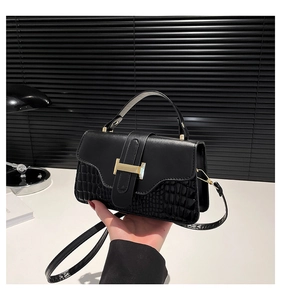 Detail view of black crocodile pattern crossbody bag with gold H-shaped clasp and handle