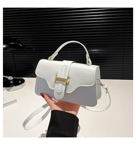 Detail of white crocodile embossed handbag with a prominent golden H-shaped buckle