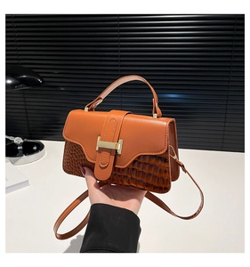 Detail of orange-brown leather bag featuring a gold H-lock and crocodile texture