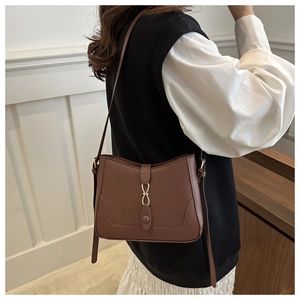 Detail of brown leather shoulder bag with gold metal buckle shown on model shoulder