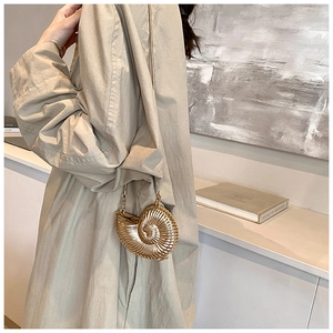 Detail of unique golden conch shell crossbody bag worn by model in minimalist interior