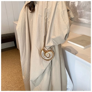 Detail of a golden seashell-shaped mini chain bag worn with a chic beige trench coat