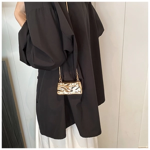Detail of a mini gold crossbody bag with ripple texture and elegant chain strap on a model