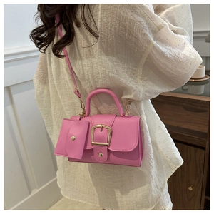 Detail of pink crossbody bag with a golden horseshoe buckle and mini coin purse pendant