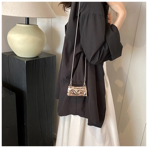 Detail of metallic pleated crossbody mini bag with chain strap on a modern lamp base