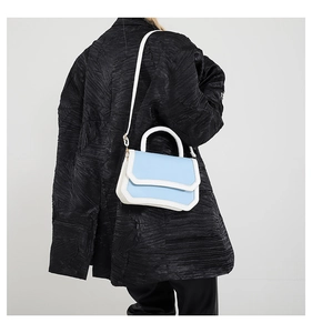 Rear view of a model wearing a small light blue and white color-block crossbody bag on a coat