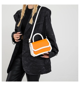 Detail of a bright orange and white crossbody bag styled on a black blazer and leather pants