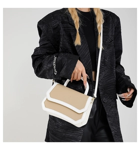 Detail of color-block flap crossbody bag with top handle and fine stitching on a model