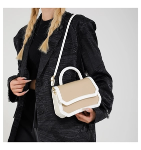 Side view of beige and white contrast flap bag worn with a textured black blazer