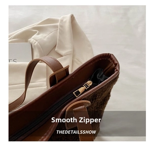 Close-up of the smooth golden zipper and brown leather trim on the plush fleece tote bag