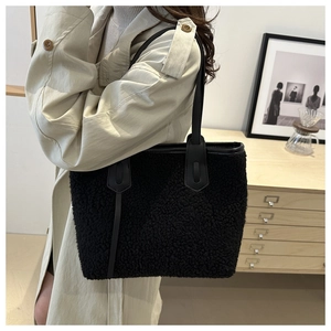 Dettaglio di una borsa tote in peluche nero con manici in pelle su una modella in trench
