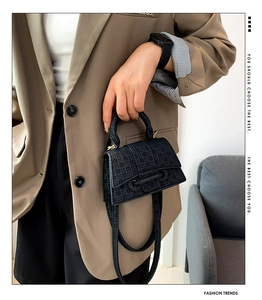 Detail of black textured crossbody bag with woven pattern held by a model in casual blazer