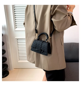 Model wearing a black quilted crossbody square bag with a gold metal strap chain