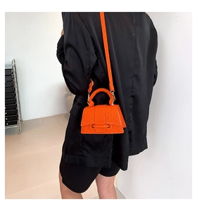 Detail of bright orange textured leather small handbag with top handle and slim strap