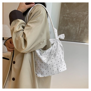 Detail of white polka dot bucket bag featuring a large lace bow on the shoulder strap