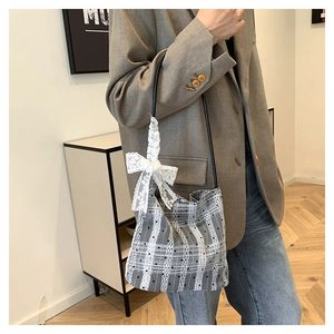Detail of grey plaid bucket bag featuring white lace trim and a decorative bow strap